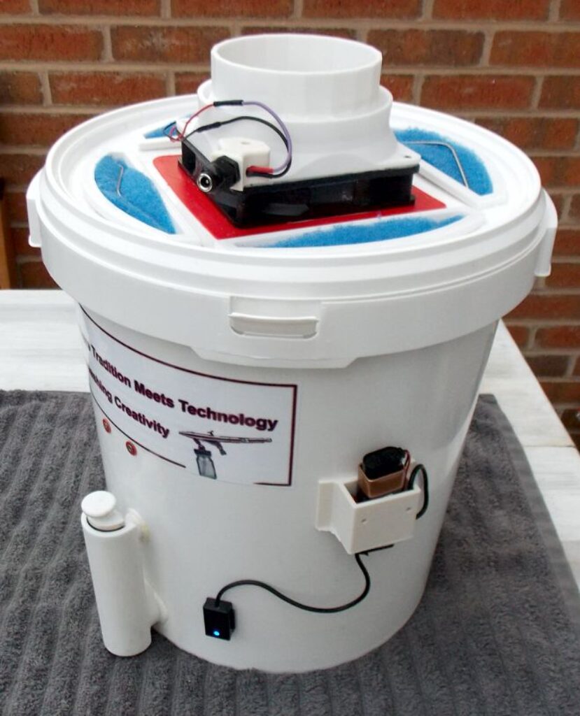 Components created through 3D printing for a hobbyist spray booth, specifically designed for indoor use, include a filtration bucket that comes with enhanced features such as an additional auxiliary fan aimed at boosting airflow. Moreover, this setup incorporates a cleaning system along with a water level sensor to ensure optimal operation and maintenance.